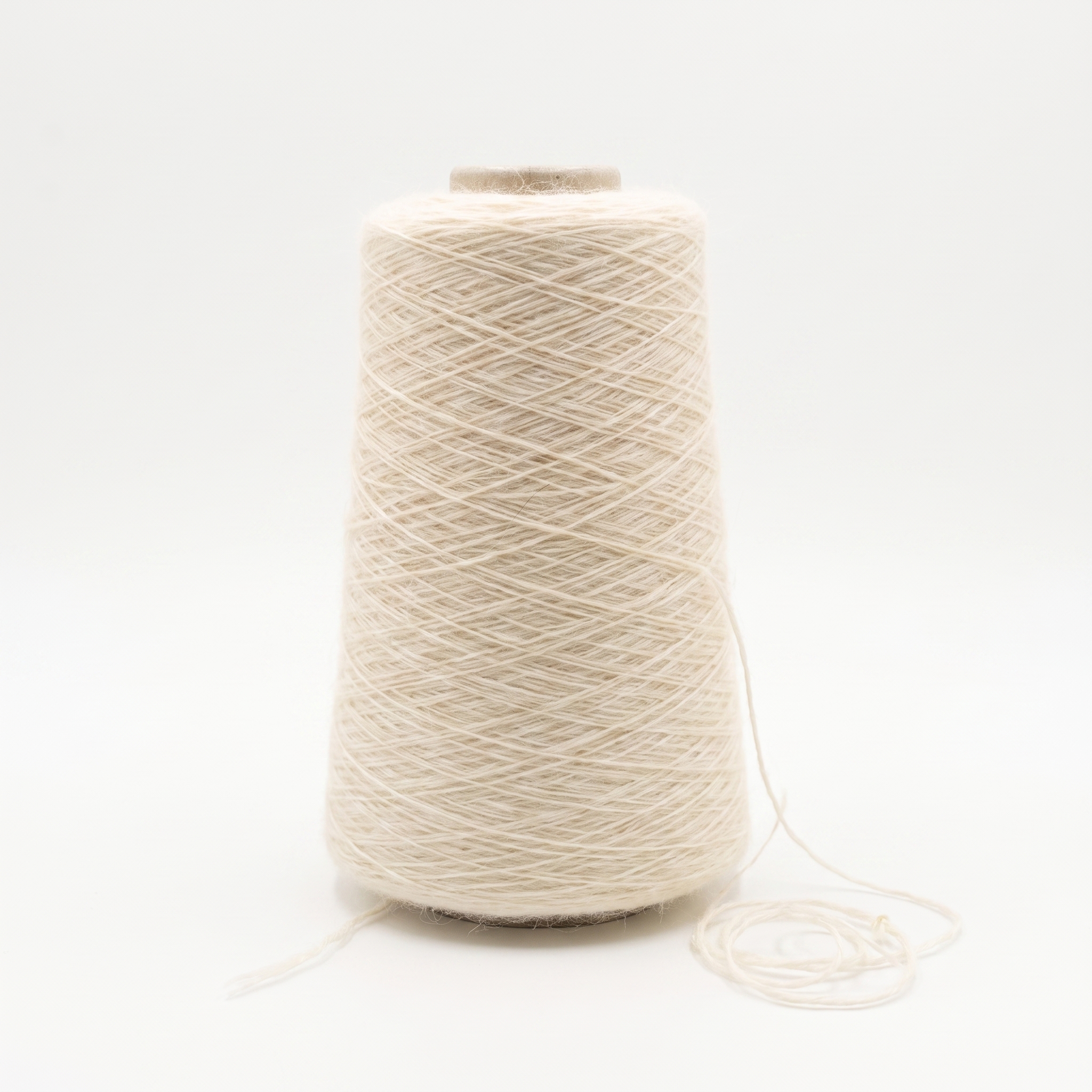 En spole med lyst beige, ullent garn og en løs tråd ved bunnen.