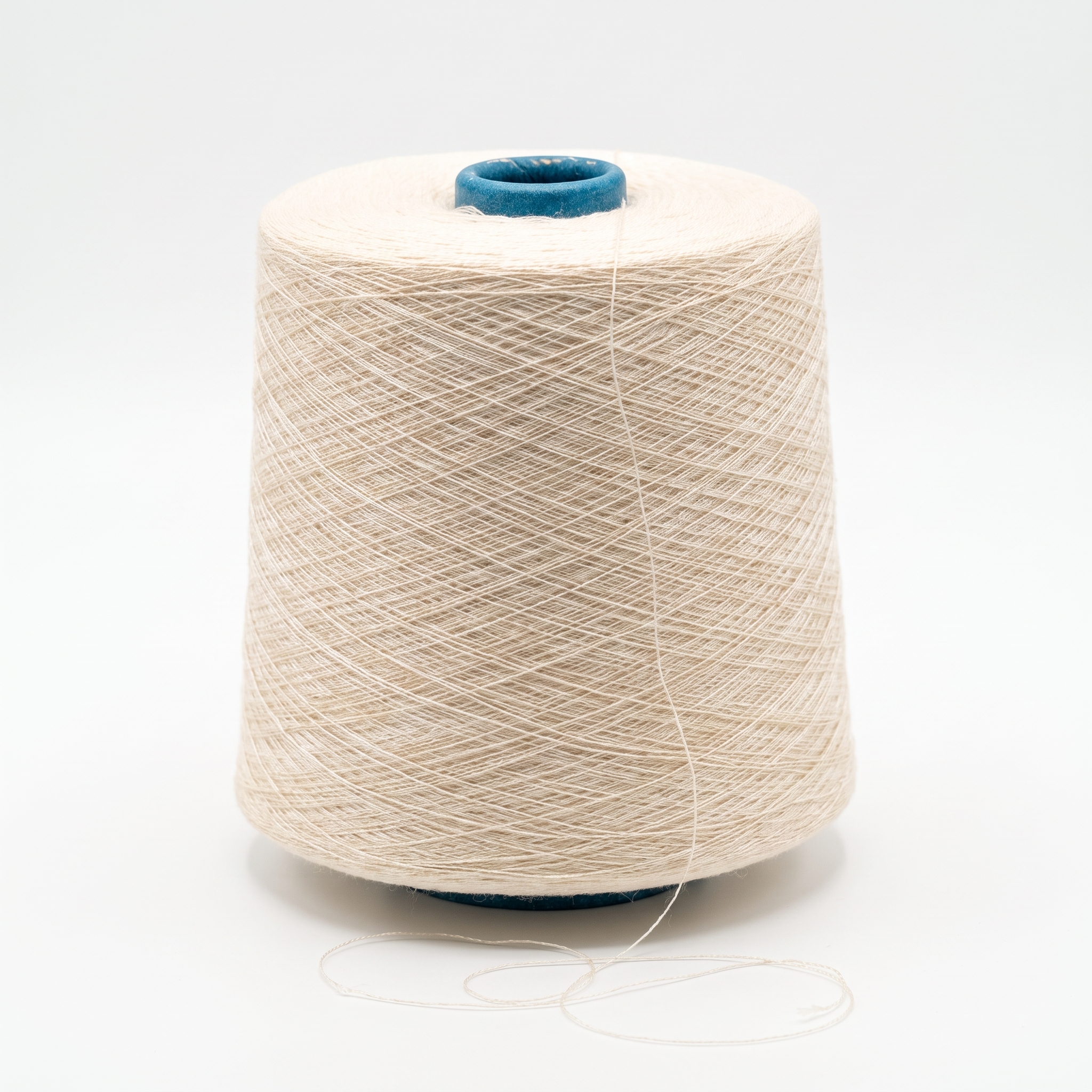 En stor spole med beige garn står på en hvit overflate, og en løs tråd ligger foran.