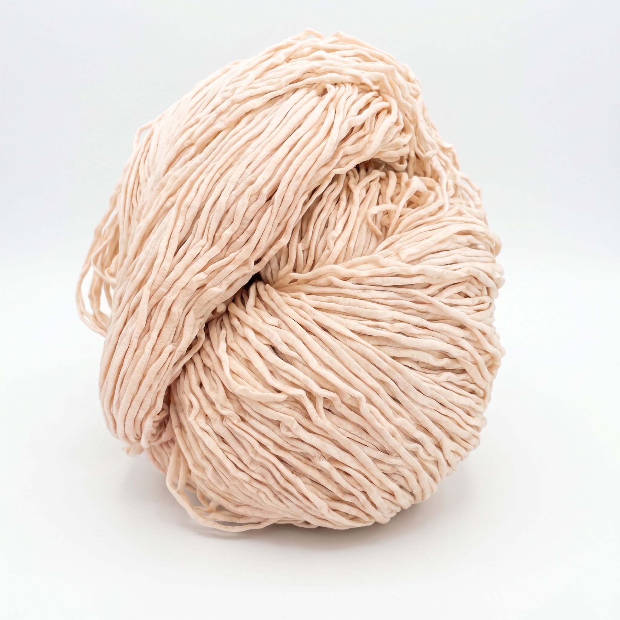 Et løst nøste av lyst beige, båndlignende garn på en hvit bakgrunn.