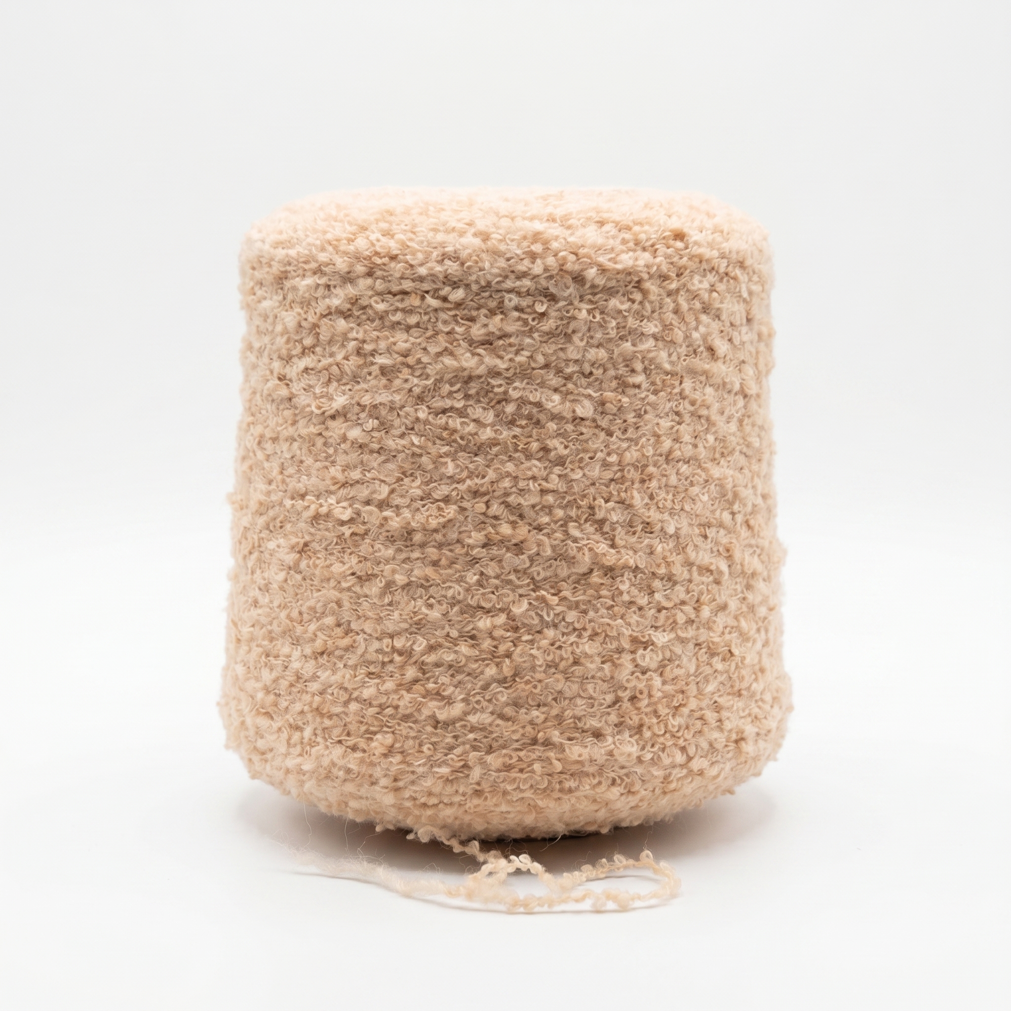 En spole med lys beige, teksturert bouclé garn på en hvit bakgrunn.