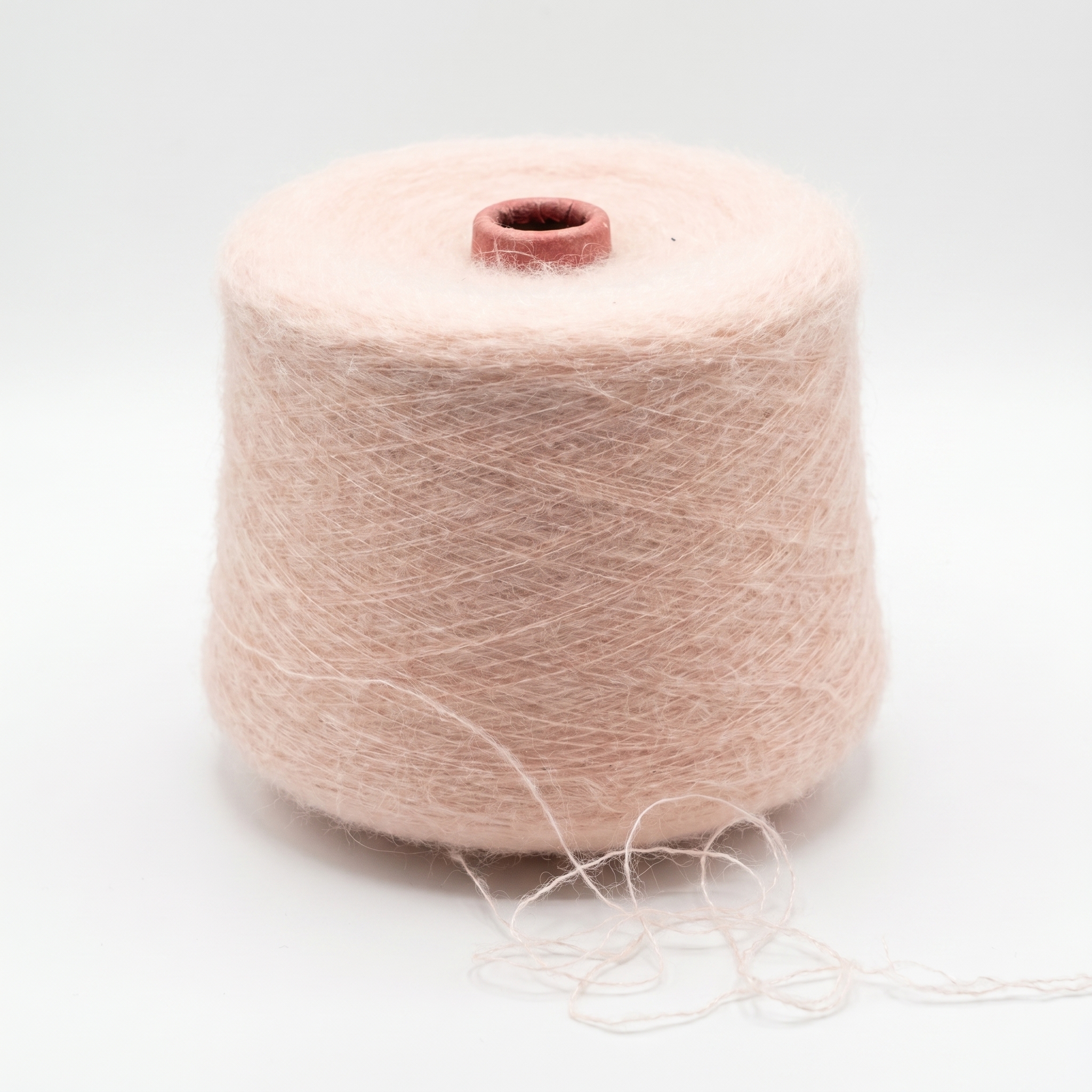 En stor spole med lyst, fluffy, rosa garn på en hvit bakgrunn med en løs tråd.