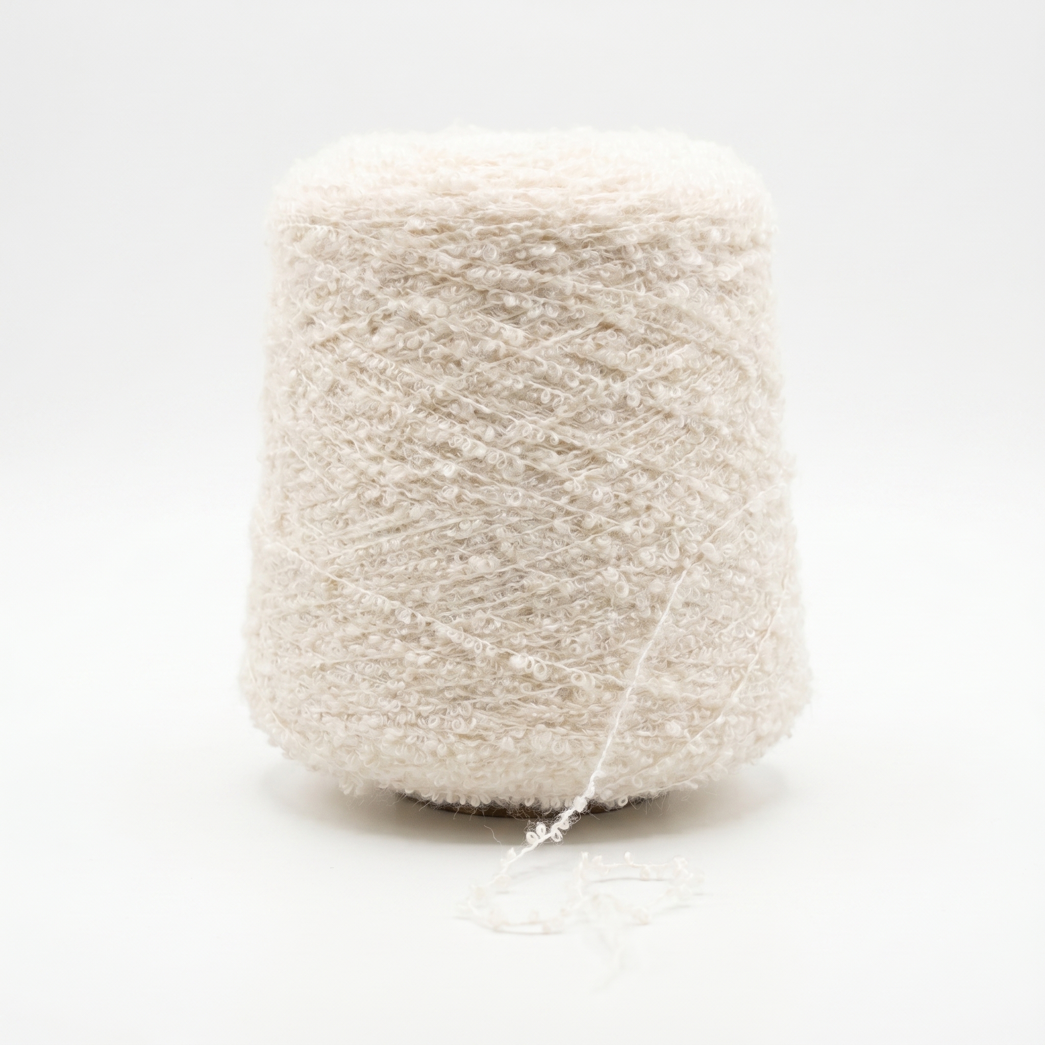 En stor spole med lyst beige, loddent bouclegarn med en løs tråd nederst.