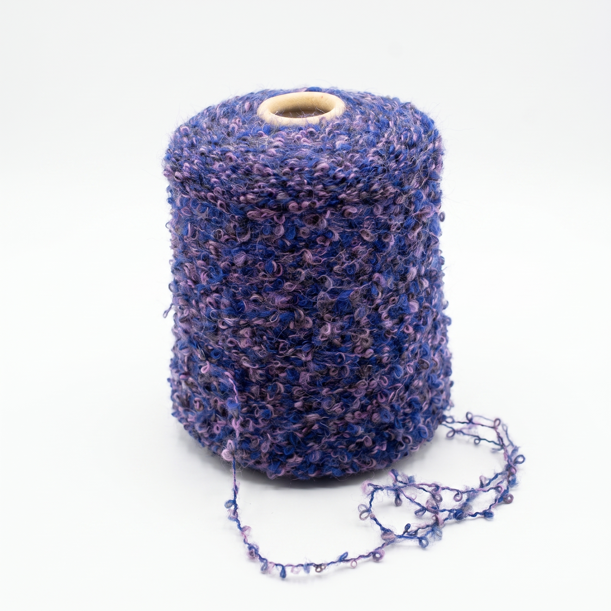 En stor spole med blått og lilla bouclé-garn på en lys bakgrunn, med en løs tråd.