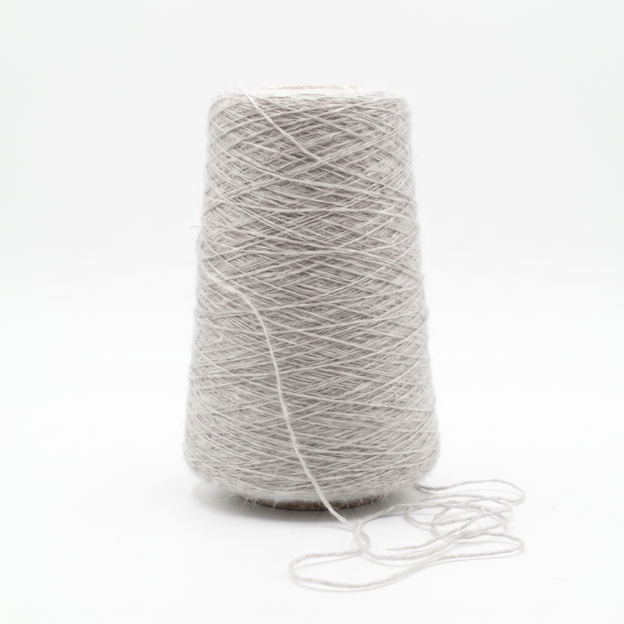 En spole med lysegrått, fiberrikt garn og en løs tråd foran på en hvit bakgrunn.